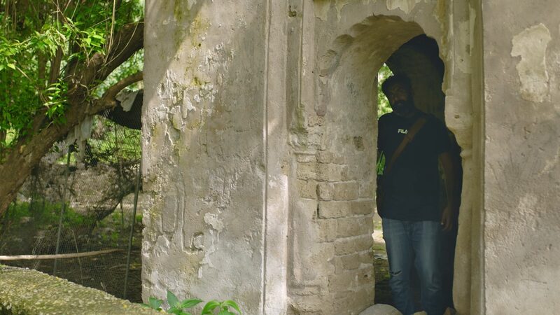 A man stands inside a crumbling white stone arch.