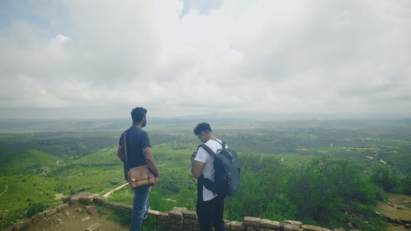 Two men with their backs to the camera look out over a green valley.